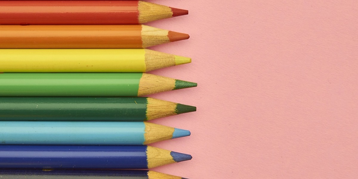 Row of coloured pencils arranged in spectrum order on a pink background