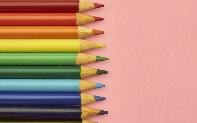 Row of coloured pencils arranged in spectrum order on a pink background