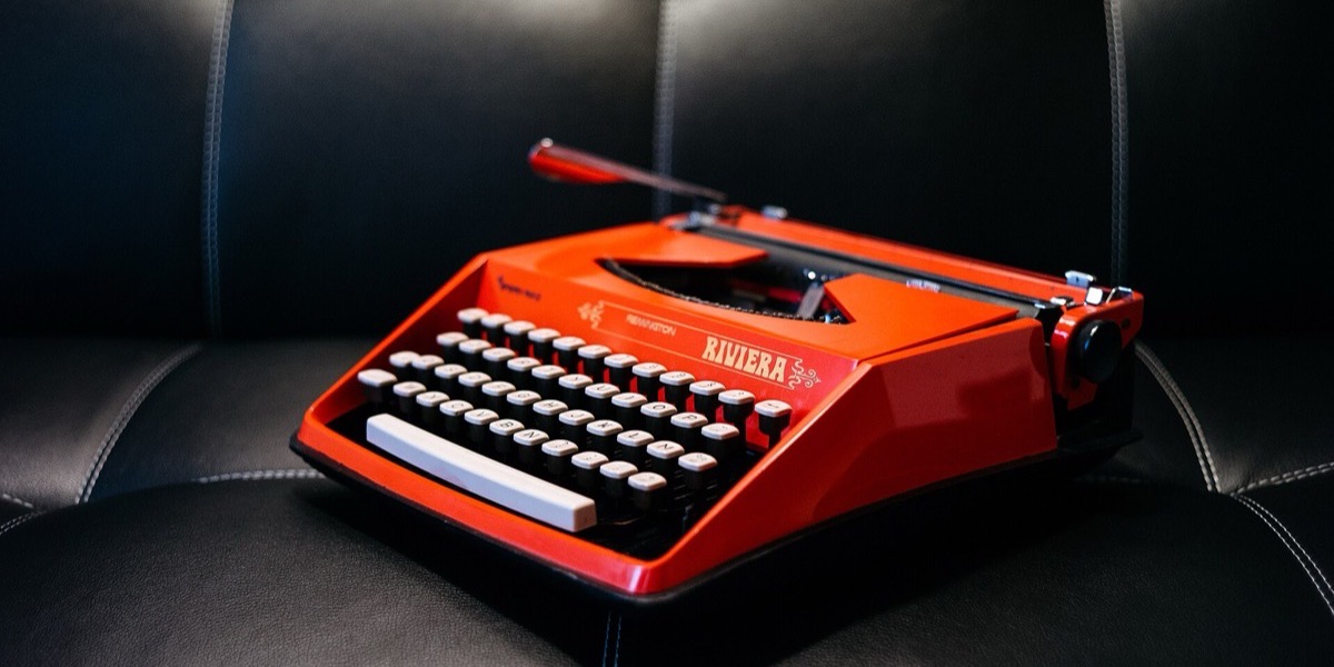 Red portable typewriter on a black leather sofa