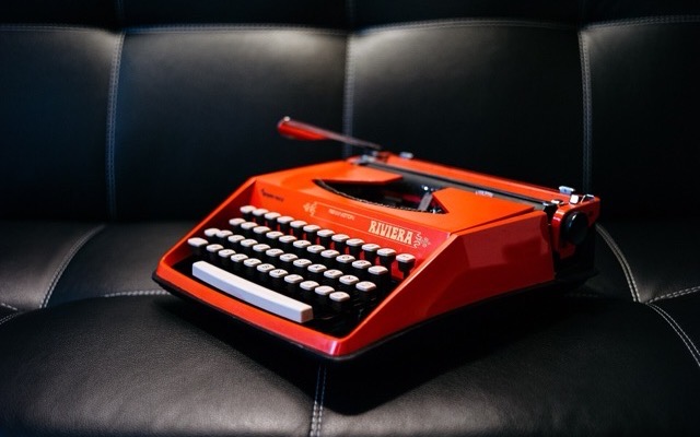 Red portable typewriter on a black leather sofa